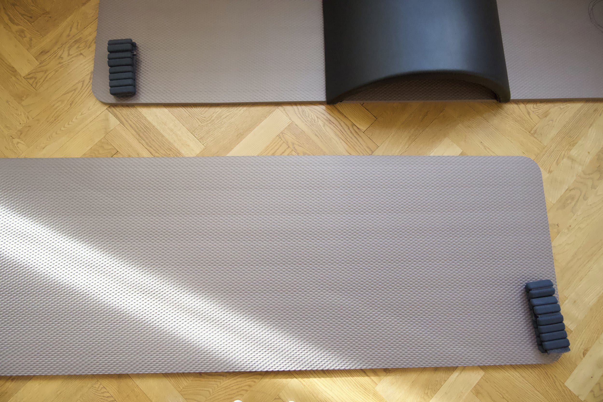 Two mats on the herringbone floor with hand weights and an arc barrel, crossed by a stripe of sunlight.